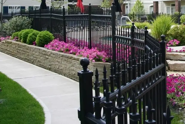 Кованый забор с каменной опорой, декорированный бордюром из садовых цветов
